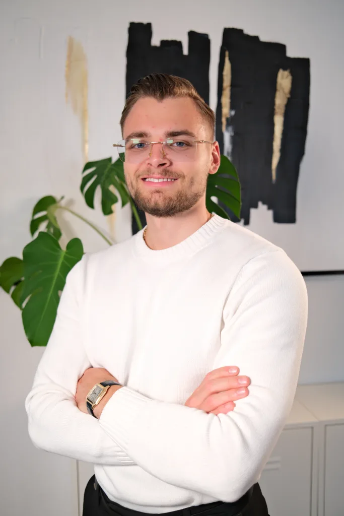 Mike Grammel, Geschäftsführer von BetonGold Immobilien, lächelt mit verschränkten Armen vor einer modernen Wanddekoration