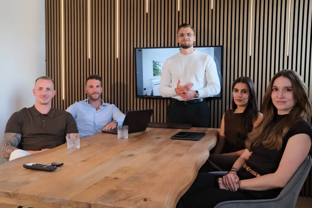 Beratungsgespräch im Konferenzraum mit Teammitgliedern von BetonGold Immobilien, am Tisch sitzend und stehend